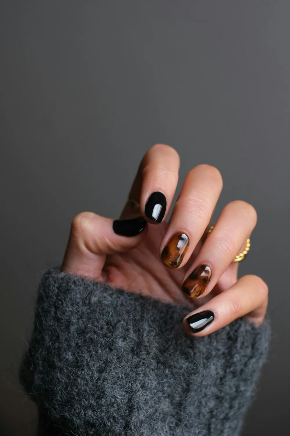 Uñas en negro y efecto carey con un anillo dorado