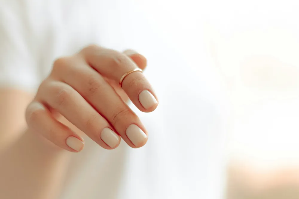 Mano con manicura blanca lechosa y un anillo fino