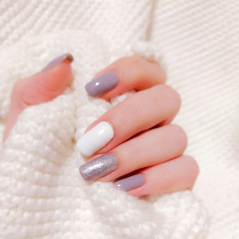 Uñas lila, blanco y glitter plateado sobre un jersey de punto