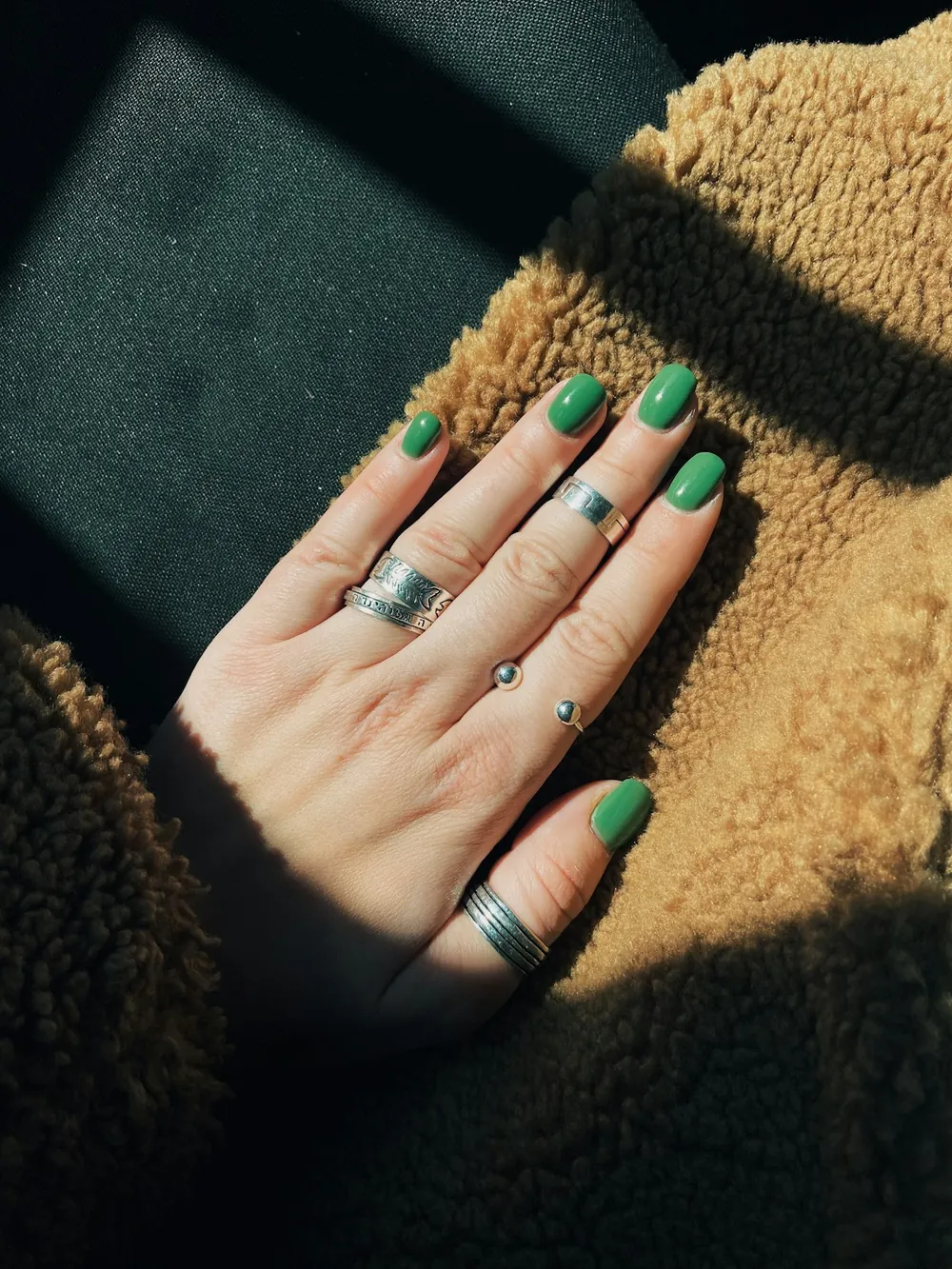Manicura verde con anillos plateados al sol